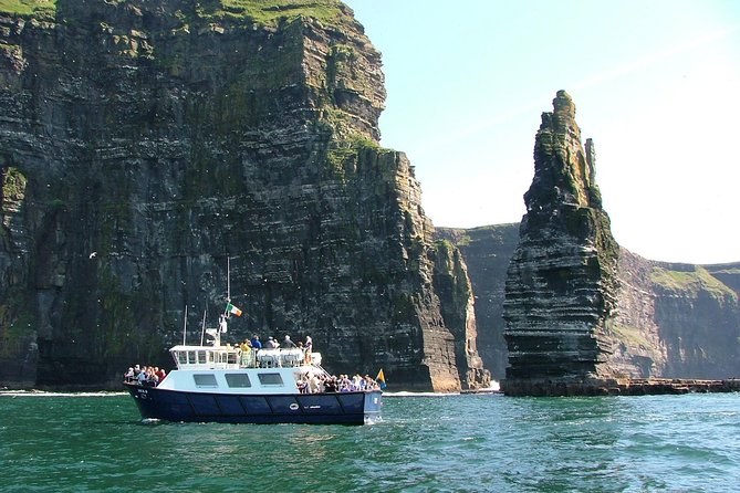 A cruise boat on the water below the Cliffs of Moher, beside the sea stack
