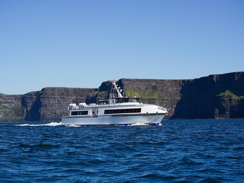 A cruise boat under the cliff wall, showing the scale of the rock above