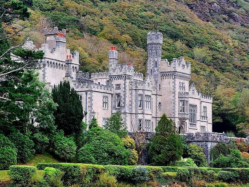 Kylemore Abbey on the lake shore beneath a wooded hillside