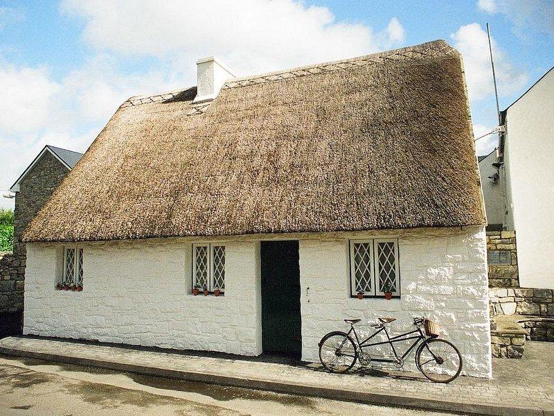 A whitewashed thatched cottage with a bicycle against the wall